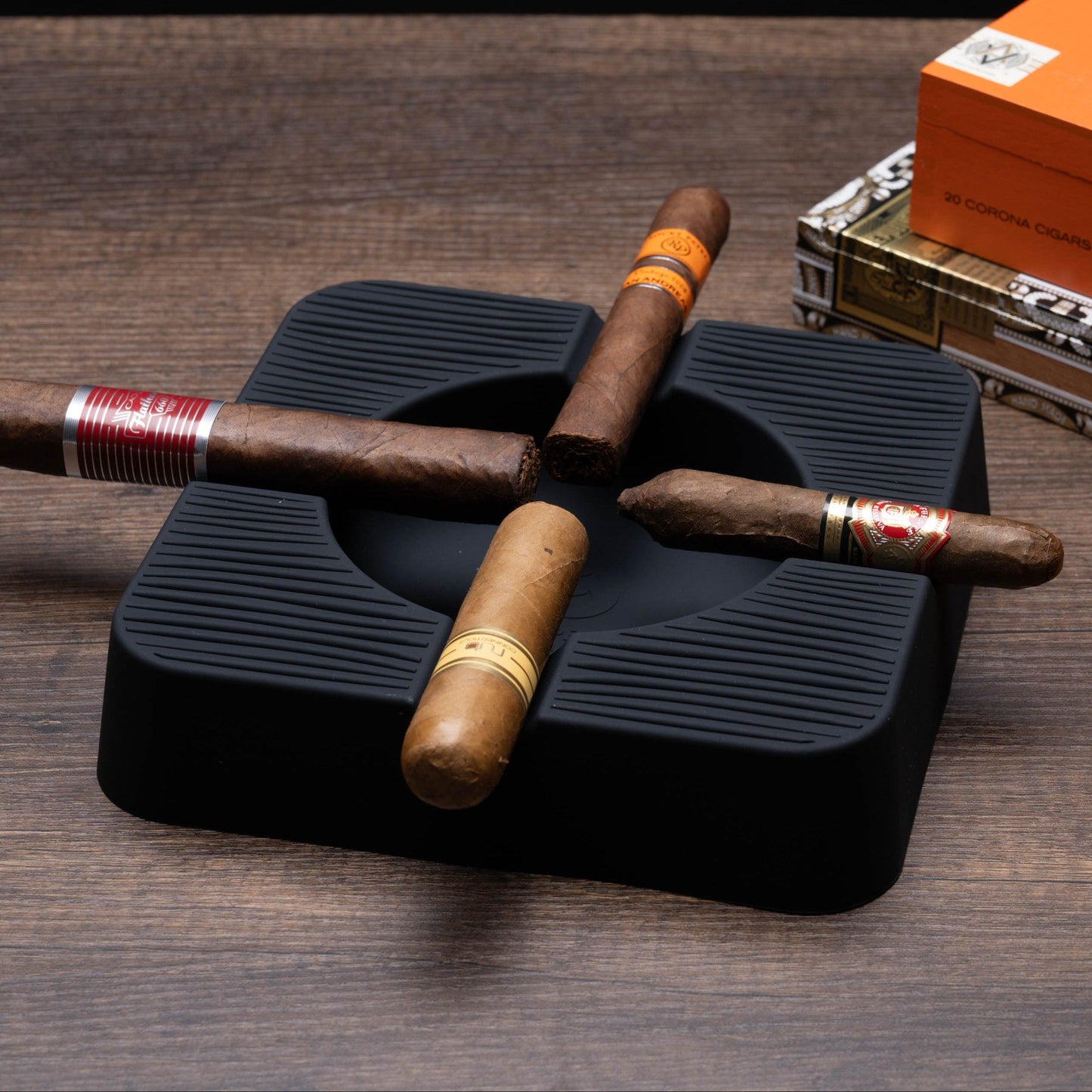 Cigars on a black humidor with a box of cigars in the background on a wooden surface