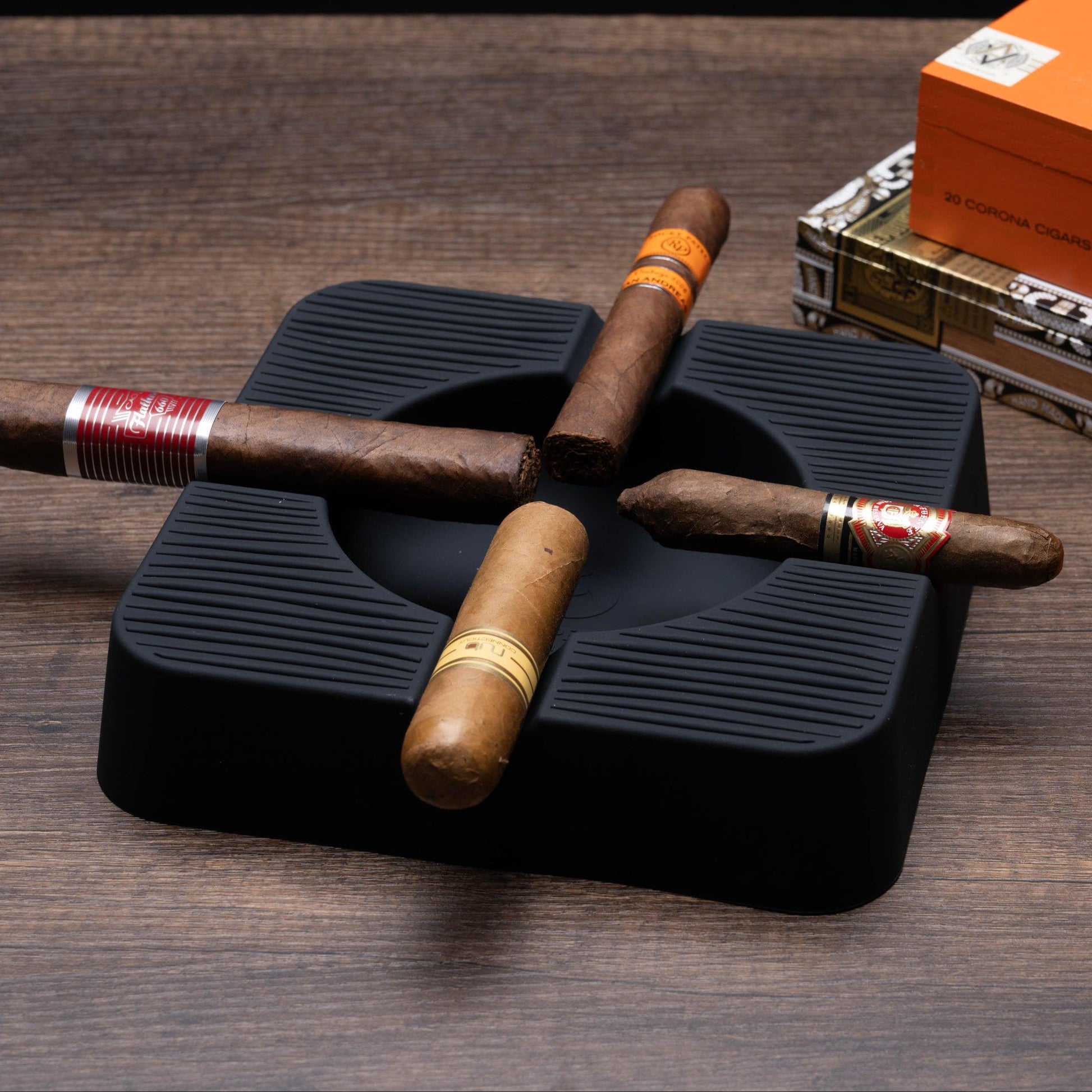 Cigars on a black humidor with a box of cigars in the background on a wooden surface