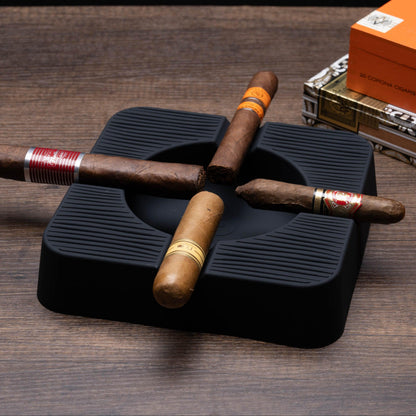 Cigars on a black humidor with a box of cigars in the background on a wooden surface