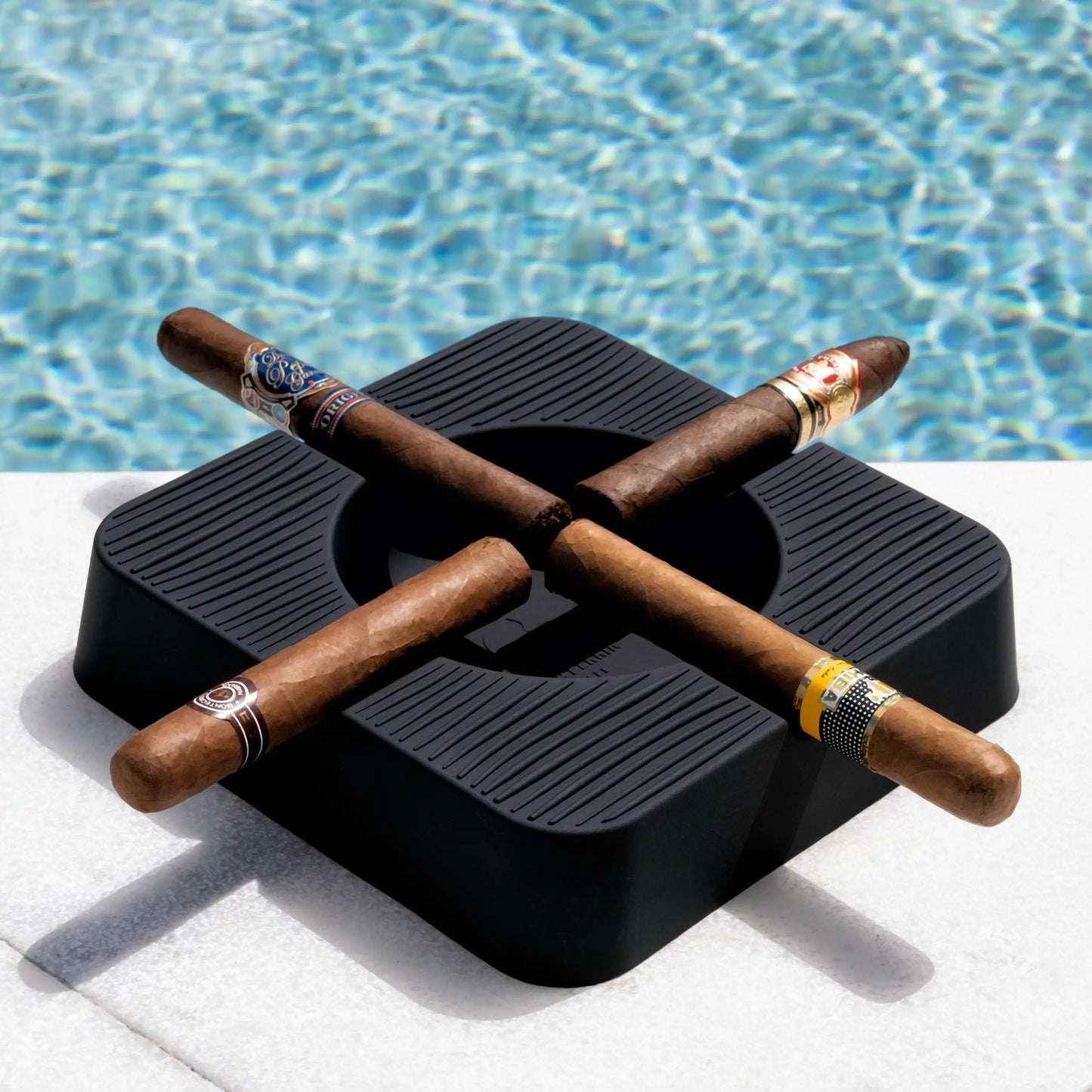 Three cigars on a black ashtray by a pool