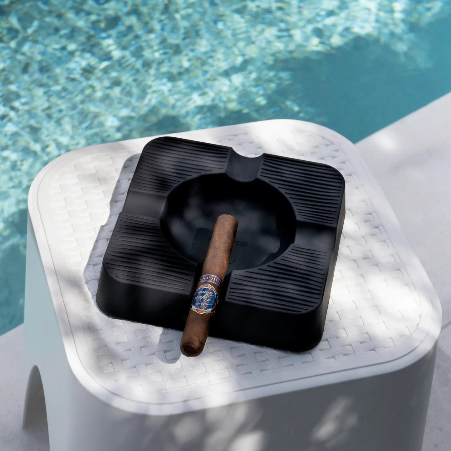 Black ashtray with a cigar on a white marble ledge by a pool
