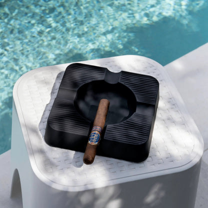 Black ashtray with a cigar on a white marble ledge by a pool